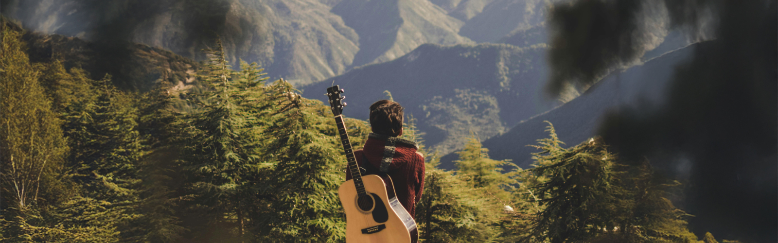 A person with a guitar looking out at a scenic view of forested hills.