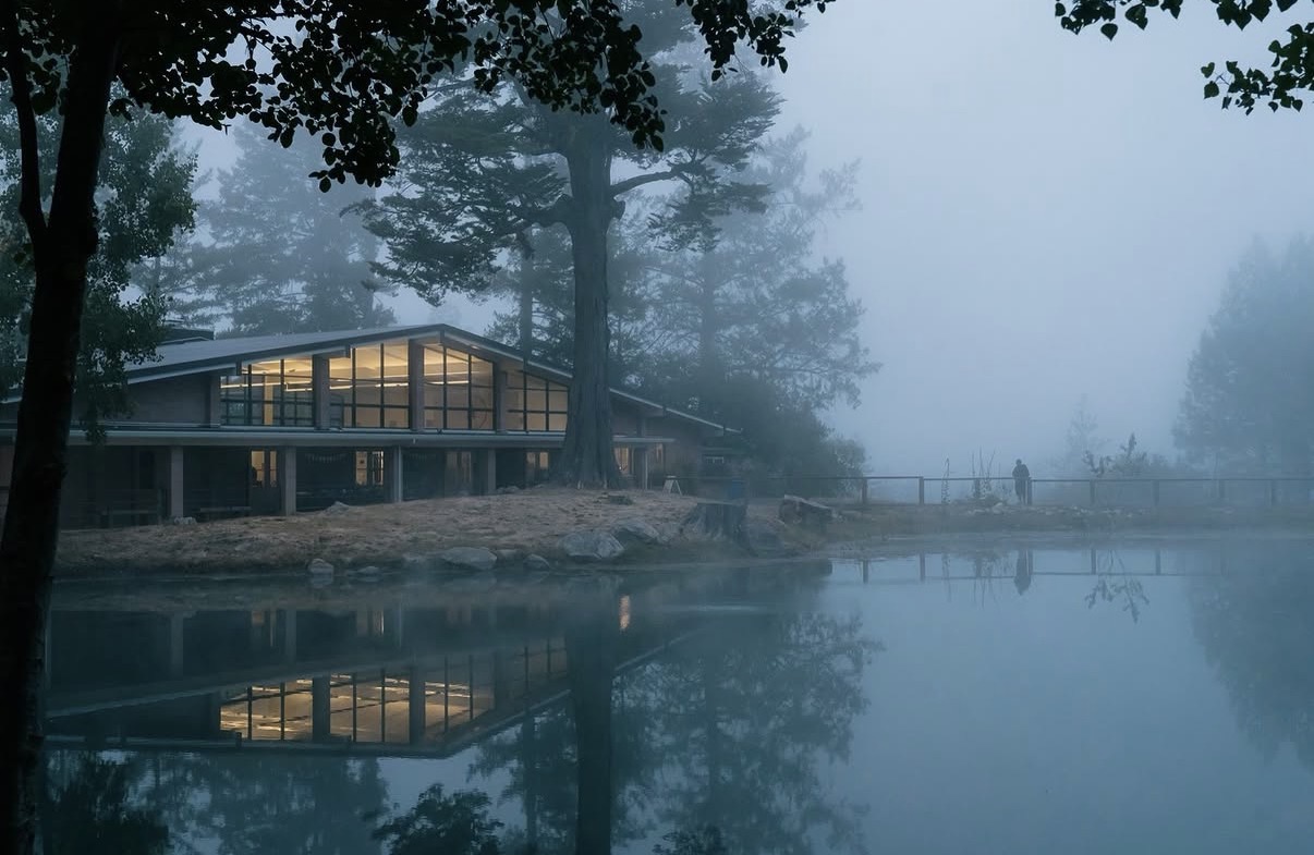 Mayacamas Dining Hall, lit up, on a grey and dewy morning, reflecting off the lake.
